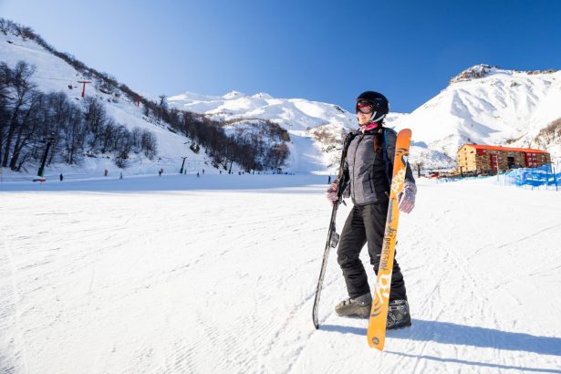 Visitante equipada para esquiar en Nevados de Chillán, rodeada de montañas nevadas y pistas de ski durante la temporada de invierno en la Región de Ñuble.